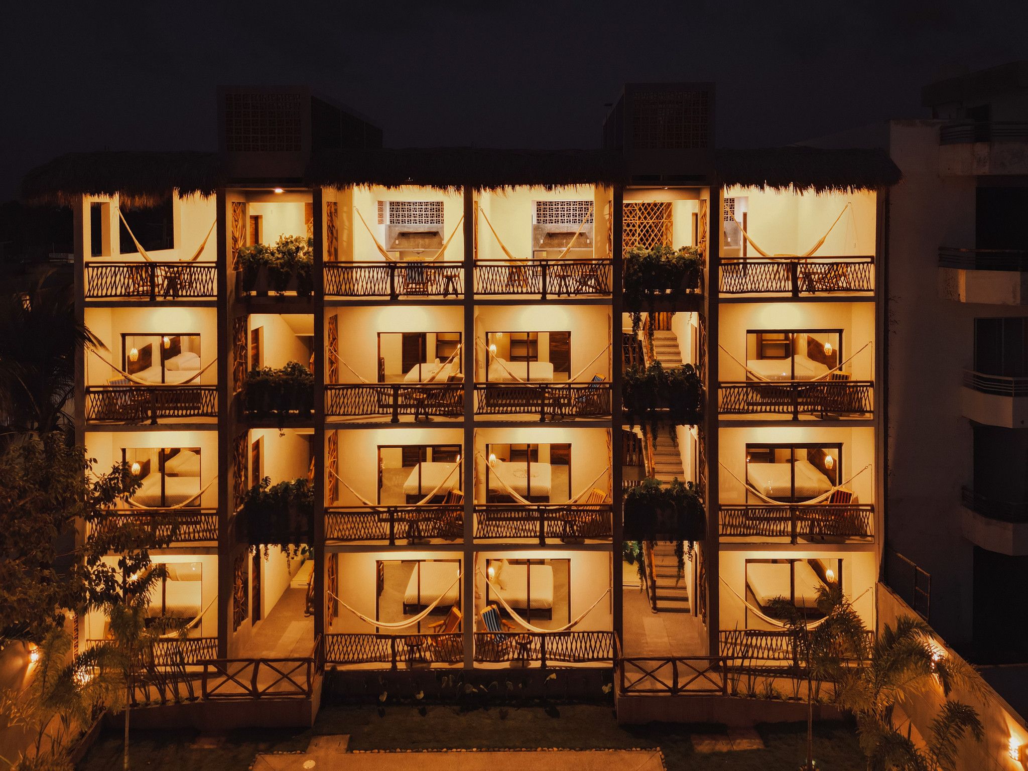 Un edificio de varios pisos con balcones, cada uno con una hamaca y plantas en macetas.