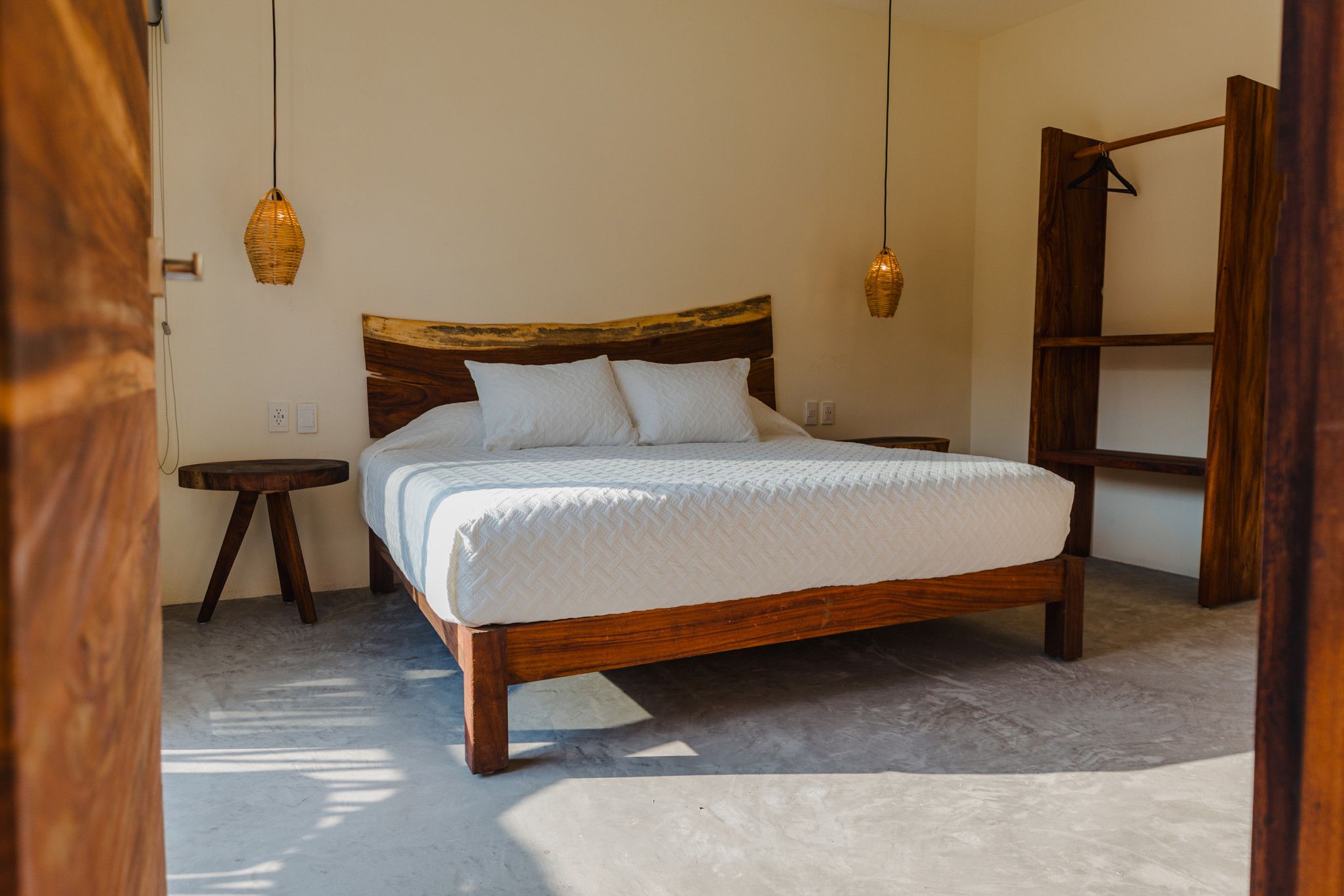Une chambre à coucher avec un lit en bois, du linge de lit blanc et deux lampes suspendues.