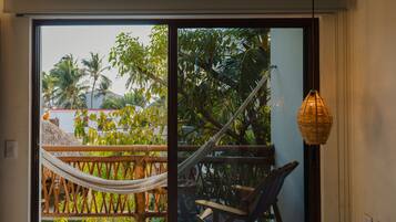 A room with a bed, a hammock, a chair, and a view of palm trees through a glass door.