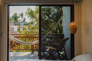 A room with a bed, a hammock, a chair, and a view of palm trees through a glass door.