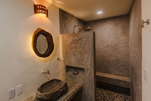 A bathroom with a stone sink, a wooden basin, a mirror, and a shower area. - Hotel Almendros Bonfil (Acapulco de Juárez)