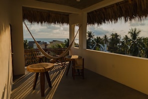 A balcony with a hammock, wooden furniture, and a view of the ocean and palm trees. - Hotel Almendros Bonfil (Acapulco de Juárez)