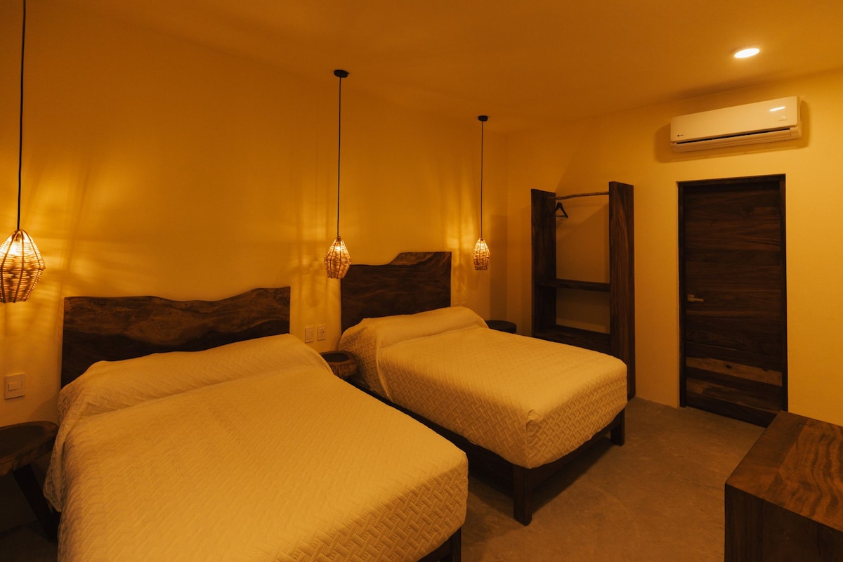 A hotel room with two beds, a wooden headboard, a hanging light fixture, an air conditioning unit, and a wooden door.