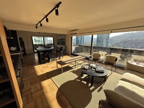 A spacious living area with a large window, a dining table, and a sofa. - Vrbo Property (Las Condes)