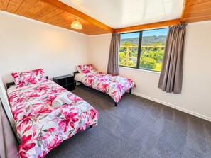 Ein Schlafzimmer mit zwei Betten, Holzboden, einem großen Fenster mit Vorhängen und Blick ins Grüne.