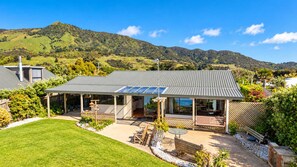 Une maison moderne dotée d’un patio couvert, d’une pelouse et offrant une vue sur des collines ondoyantes.