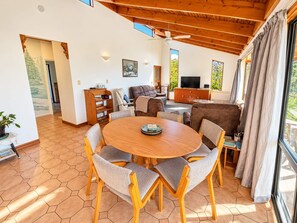 A spacious living area with a round wooden table, multiple chairs, a sofa, and a television. - Pakawau Beach - Ratrace Retreat (Pākawau)