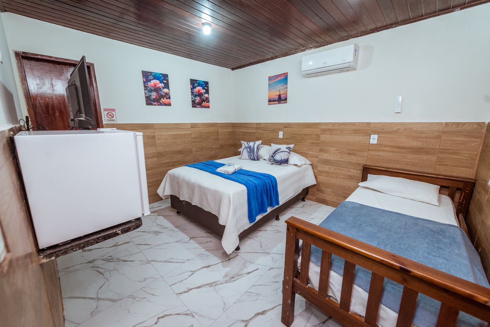 A room with two beds, a wooden ceiling, a white air conditioner, and a refrigerator.