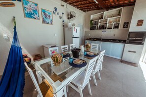 Un coin repas avec une table en verre, des chaises blanches et un hamac bleu.