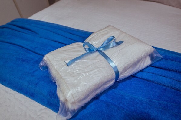 Ein Bett mit einer blauen Decke und einem in Plastik verpackten Kopfkissen, das mit einem blauen Band verschnürt ist.