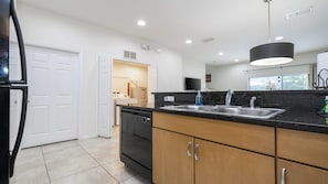 A modern kitchen with a black countertop, stainless steel sink, and wooden cabinets. - Near Disney Cozy 2BR Townhouse with Hot Tub (Kissimmee)
