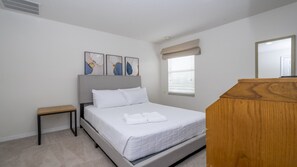 A bedroom with a bed, a nightstand, a wooden dresser, and a window with blinds. - Near Disney Cozy 2BR Townhouse with Hot Tub (Kissimmee)