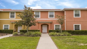 A two-story residential building with a central entrance, a small tree in front, and a clear sky. - Near Disney Cozy 2BR Townhouse with Hot Tub (Kissimmee)
