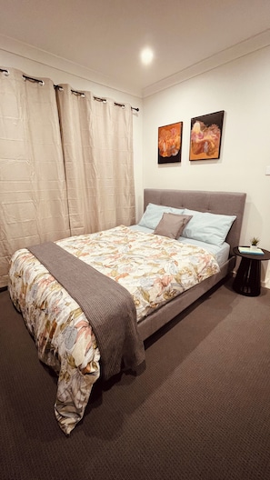 A bedroom with a bed, curtains, two wall art pieces, a small table with a plant, and a carpeted floor. - Coast, Canopy & City: Cozy 2-bedroom Home (Gilead)
