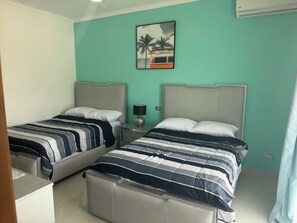 A hotel room with two beds, a nightstand, a lamp, and a painting on the wall. - An exquisite an exceptional, 5 star resorts style condominium complex (Punta Cana)