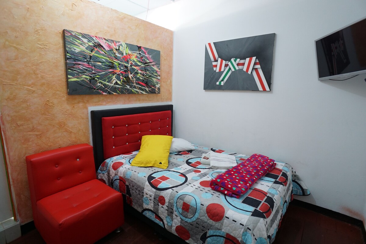 A bedroom with a bed, a red chair, two paintings, and a television.