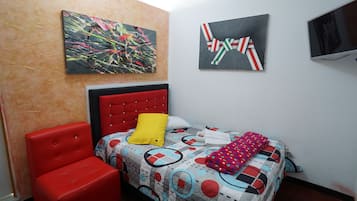 A bedroom with a bed, a red chair, two paintings, and a television.