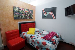 A bedroom with a bed, a red chair, two paintings, and a television. - Hotel Arte  (SANTA ROSA DE CABAL)