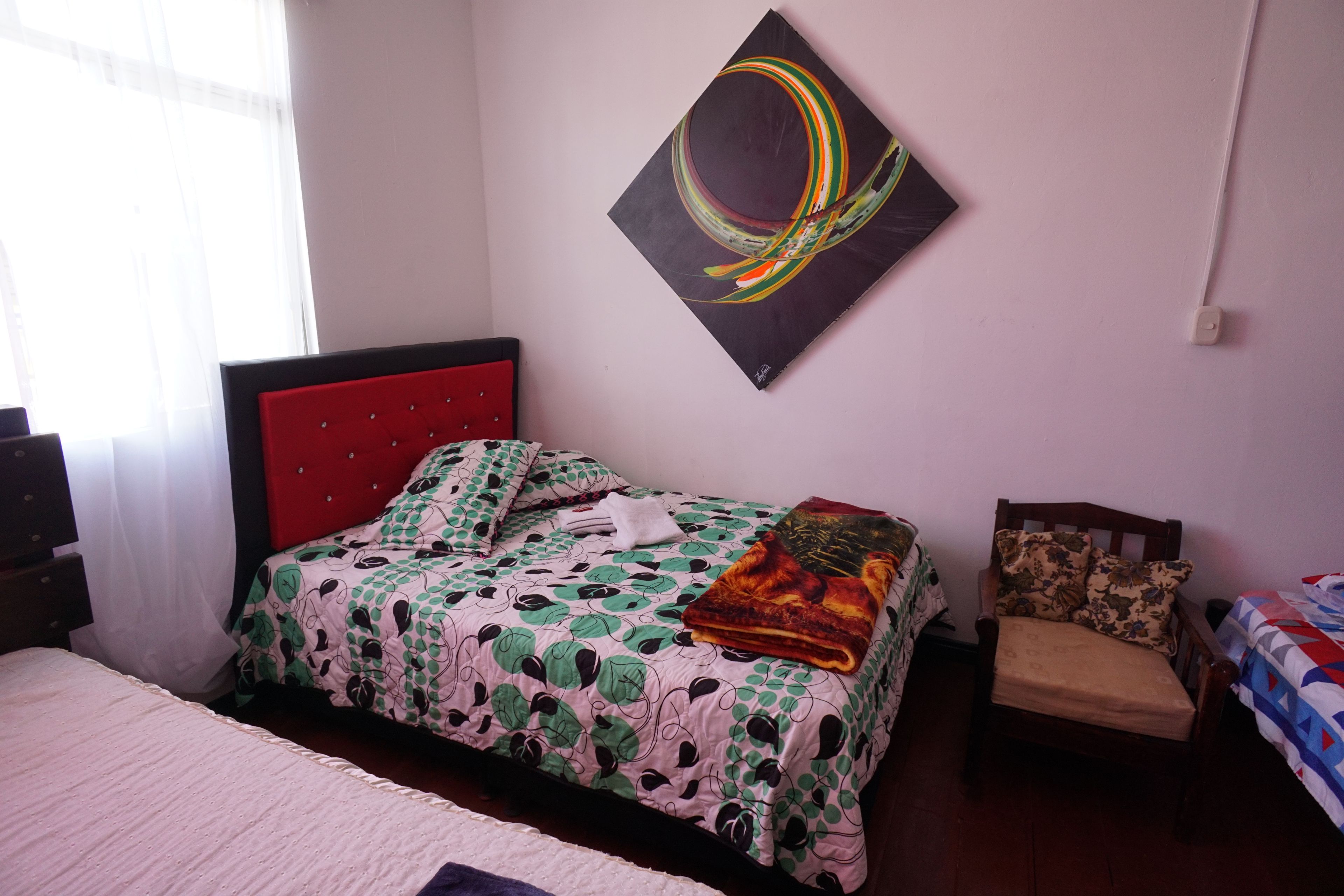 Un dormitorio con cama, una silla, un cuadro y una ventana.