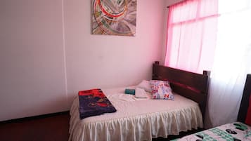 A bedroom with a single bed, a bedside table, a wall painting, and a window with curtains.