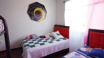 A bedroom with a bed, a window with curtains, and a wall-mounted artwork.