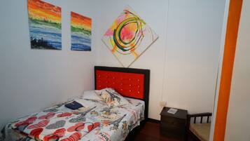 Un dormitorio con cama, mesita de noche, cajón y dos cuadros en la pared.