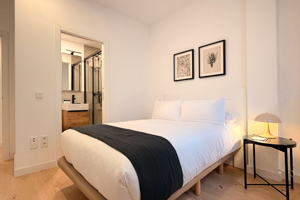 A bedroom with a bed, bedside table, lamp, and two framed pictures on the wall.