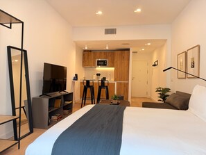 A modern hotel room with a large bed, a TV, a kitchenette, and a seating area with bar stools. - Monteleón Apartments by Wynwood (Madrid)
