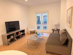 A modern living room with a flat-screen TV, a sofa, a coffee table, and a bookshelf. - Monteleón Apartments by Wynwood (Madrid)