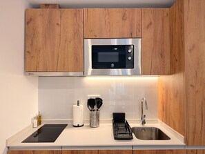 A modern kitchen with wooden cabinets, a stainless steel microwave, a black induction cooktop, a sink, and a utensil holder. - Monteleón Apartments by Wynwood (Madrid)