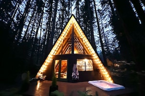 Eine dreieckige Holzhütte mit geneigtem Dach, umgeben von einem Wald.