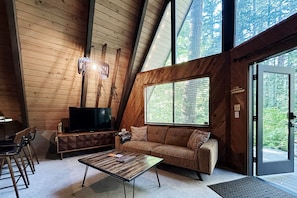 Ein gemütliches Blockhaus-Interieur mit Holzbalkendecke, einer Couch, einem Couchtisch und einem Fernseher.