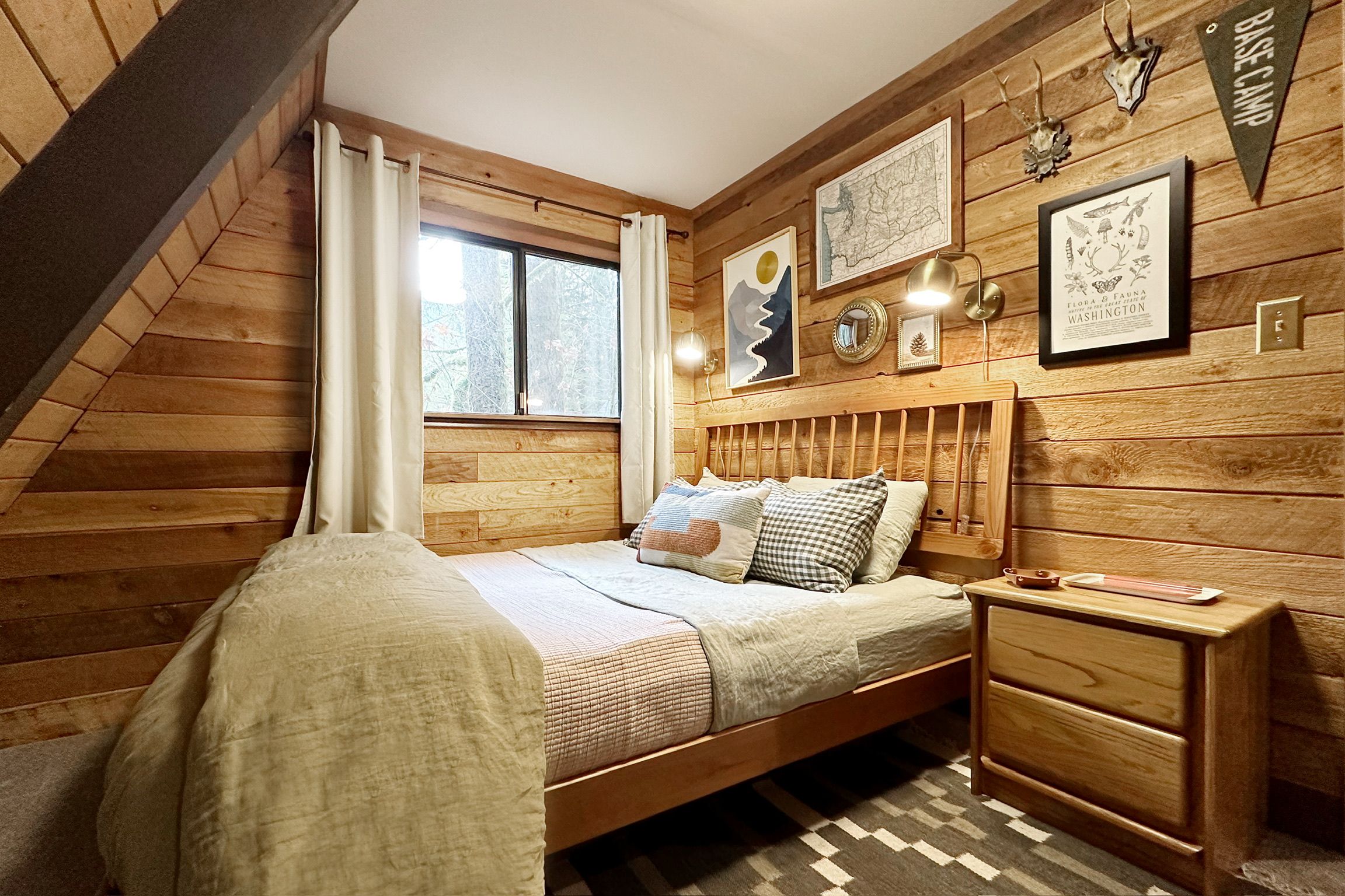 Ein Schlafzimmer mit Holzbalkendecke, einem Bett mit vielen Kissen, einem Nachttisch und Wanddekoration, darunter eine Karte und ein gerahmtes Bild.
