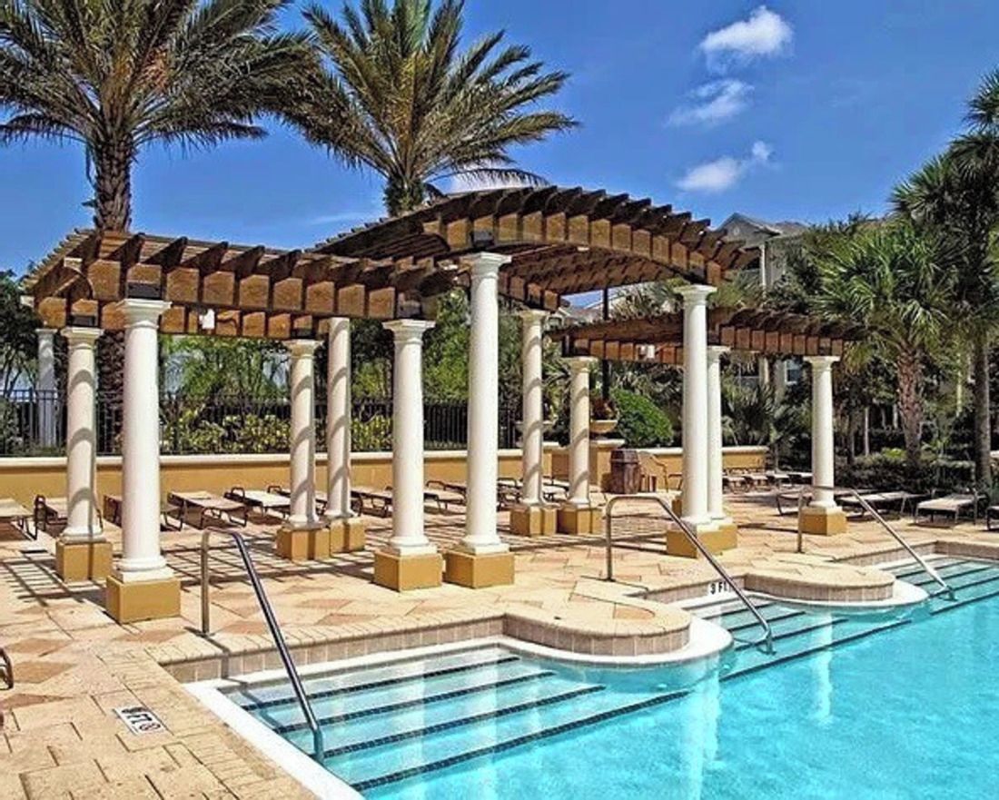 Un área de piscina con una pérgola, palmeras y sillones de descanso.