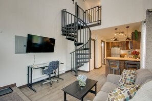 Un salon moderne avec un escalier à volutes, un téléviseur à écran plat, un bureau avec une chaise et un canapé.