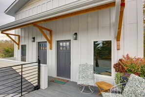 A covered porch with a wooden railing, a gray door, and a window. - Livingston Loft | Mountain Views Near Downtown (Livingston)