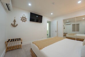 Een slaapkamer met een bed, een aan de muur bevestigde televisie, een houten stoel en een kledingkast met spiegel.