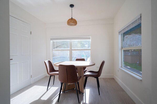 Un'area pranzo con un tavolo rotondo e sei sedie, un'ampia finestra che si affaccia su un giardino e un lampadario al soffitto.