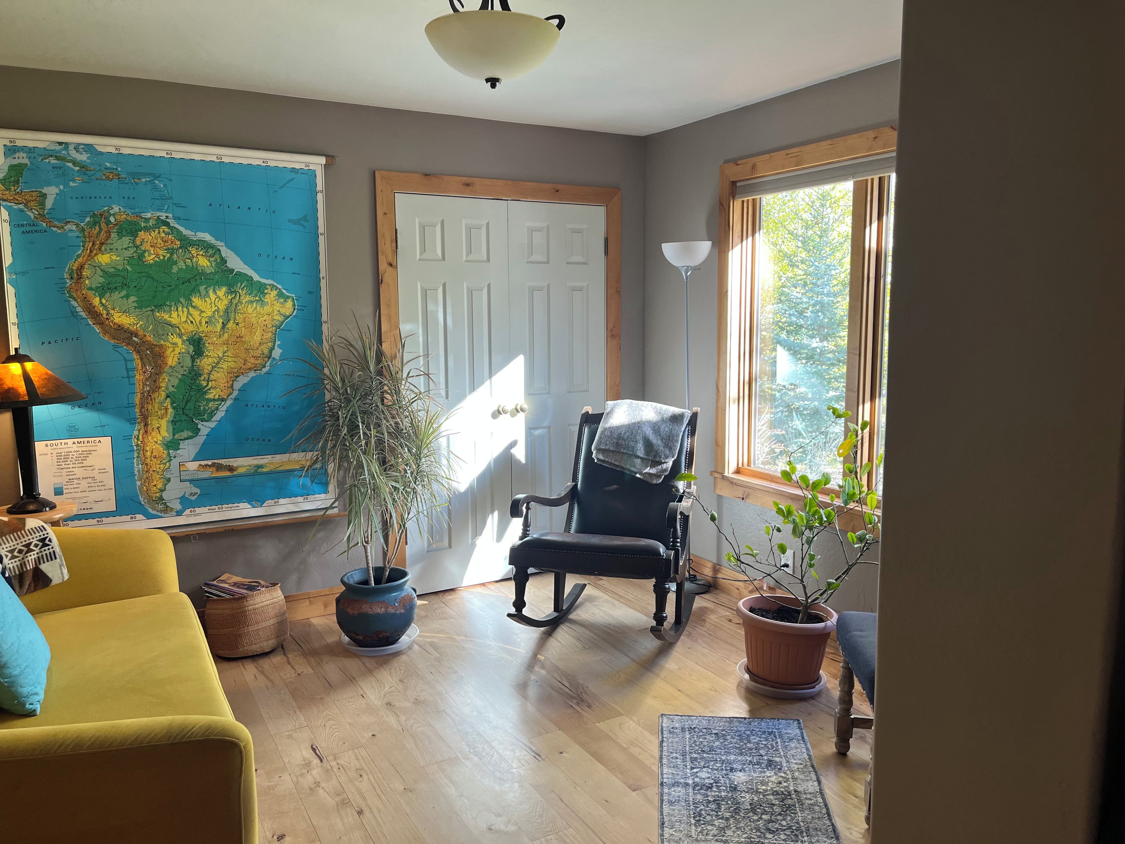 Una habitación con un mapa grande, una silla, un sofá y una ventana que da a zonas verdes.