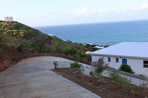 A coastal road with a white building and a view of the sea. - Modern 2BR St Croix Home with an Amazing Ocean View (Christiansted)