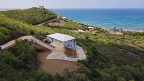 A single-story building with a flat roof, surrounded by a landscaped area with a curved driveway. - Modern 2BR St Croix Home with an Amazing Ocean View (Christiansted)