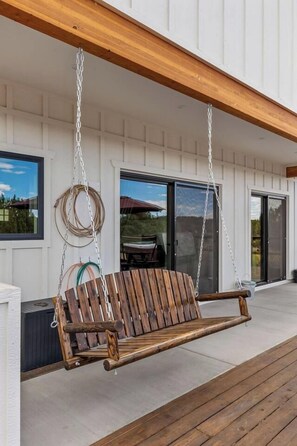 A wooden swing suspended from a ceiling in a covered outdoor area with a concrete floor. - Outlaw Rest | Hot Tub, Pickleball, Views, Game Room, Poker, Grand Canyon (Williams)