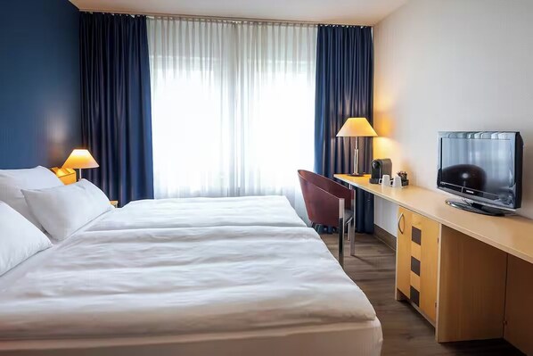 Ein Hotelzimmer mit zwei Betten, einem Schreibtisch, einem Fernseher und einem Sessel.