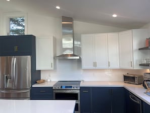 A modern kitchen with stainless steel appliances, white cabinets, and a central island. - Bright + spacious home w/ sauna. Steps to ocean, bluff-top trail, and downtown (Half Moon Bay)
