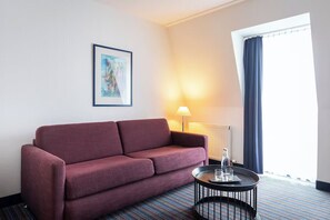 Ein Zimmer mit einer Couch, einer Lampe, einem kleinen Tisch mit Gläsern, einem Heizkörper und einem Fenster mit Vorhängen.