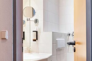 Ein Badezimmer mit Waschbecken, runder Spiegel, Handtuchspender und Toilettenpapierhalter.