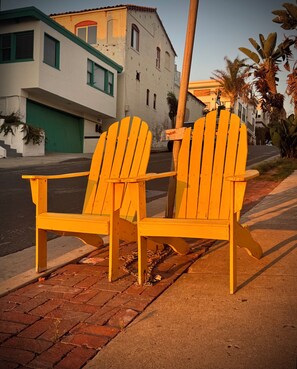 Two yellow Adirondack chairs on a brick sidewalk with a street and buildings in the background. - Boutique Surf Hideaway Steps from the Pacific (Manhattan Beach)