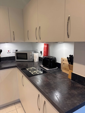 A kitchen with a microwave, toaster, and a cutting board with knives. - Charming Ground Floor Apartment Near Beach, Norfolk (Sheringham)