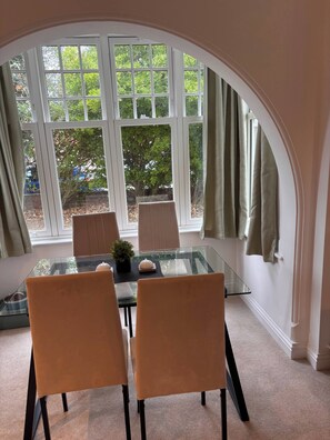 A dining area with a glass table, two chairs, and a view through large windows. - Charming Ground Floor Apartment Near Beach, Norfolk (Sheringham)