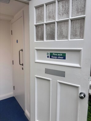A white door with a fire exit sign and a keep clear sign, a metal handle, and a blue carpeted floor. - Charming Ground Floor Apartment Near Beach, Norfolk (Sheringham)